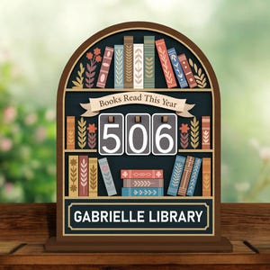 Może przedstawiać: Drewniany znak w kształcie półki na książki z napisem "Books Read This Year" i numerem "506". Znak zawiera również tekst "GABRIELLE LIBRARY" i dekoracyjne ilustracje książek. Znak jest brązowy z czarnym tłem.