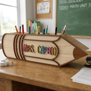 Może przedstawiać: Drewniany organizer na biurko w kształcie ołówka z napisem "MRS. CAPRIO" w kolorowych literach. Organizer posiada wiele przegródek na długopisy i ołówki. Projekt wykonany jest z jasnego drewna z ciemnobrązowymi obramowaniami.