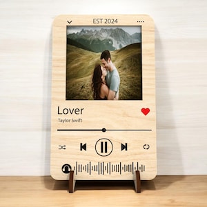 May include: Wooden photo frame with a picture of a couple, designed to resemble a music player interface. The frame includes the word "Lover" and the artist's name, a red heart icon, and the text "EST 2024".