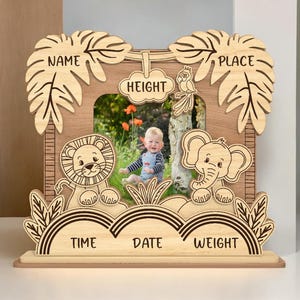Peut inclure: Cadre photo en bois sur le thème de la jungle. Il comporte des espaces pour une photo, un nom, un lieu, une heure, une date, un poids et une taille. Le cadre présente un lion, un éléphant et des feuilles de palmier.