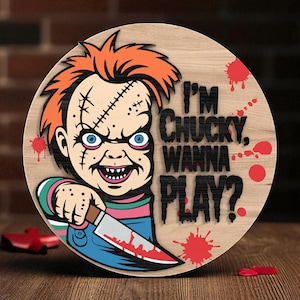 以下が含まれることがあります： オレンジ色の髪、青い目、縫い目のあるチャッキーの漫画の画像が描かれた丸い木製の看板。看板には「I'M CHUCKY, WANNA PLAY？」というテキストと赤い血しぶき、ナイフが含まれています。