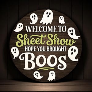 Puede incluir: Un letrero redondo de madera con el texto "WELCOME TO Sheet Show HOPE YOU BROUGHT BOOS" en letras blancas y verdes. Siluetas de fantasmas blancos rodean el texto. El letrero est&aacute; sobre un fondo de madera oscura, ideal para Halloween.