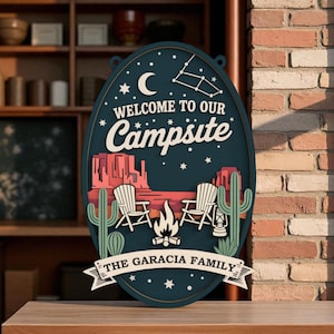 May include: Oval-shaped wooden sign with a dark blue background, featuring the text "Welcome to our Campsite" and "The Garcia Family." The sign includes a desert landscape with cacti, chairs, a campfire, and a lantern.