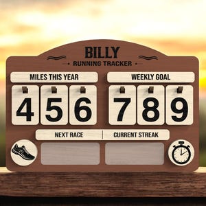 May include: A wooden running tracker with the name "BILLY" at the top. It displays "MILES THIS YEAR" as 456 and "WEEKLY GOAL" as 789. Includes a running shoe icon and a stopwatch icon. The text "RUNNING TRACKER" is also visible.