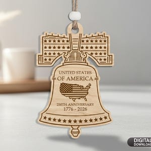 May include: A wooden bell-shaped ornament featuring the text "UNITED STATES OF AMERICA" and a map of the USA with the American flag. The ornament commemorates the "250TH ANNIVERSARY 1776-2026". It has a string for hanging.