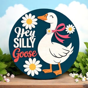 Könnte beinhalten: Ein rundes Holzschild mit marineblauem Hintergrund zeigt eine weiße Gans mit orangefarbenem Schnabel und Füßen, verziert mit einer rosa Schleife und Gänseblümchen. Die Worte "Hey Silly Goose" sind in Weiß und Rot geschrieben.