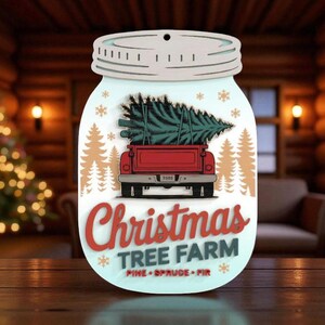 Op de afbeelding: Houten kerstornament in de vorm van een weckpot. Het toont een rode vrachtwagen die een kerstboom vervoert, met de tekst "Christmas Tree Farm" in rood en wit. Het ornament vermeldt ook Pine, Spruce en Fir.