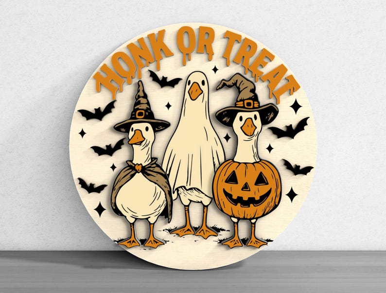 Puede incluir: Decoraci&oacute;n redonda de Halloween de madera con tres gansos disfrazados. Uno es un fantasma, otro una bruja y otro una calabaza. Las palabras "HONK OR TREAT" est&aacute;n en la parte superior, con murci&eacute;lagos y estrellas alrededor de los gansos.