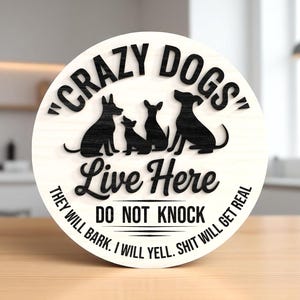 May include: A round wooden sign with the text "CRAZY DOGS Live Here" and the silhouettes of three dogs. The sign also includes the phrases "THEY WILL BARK. I WILL YELL. SHIT WILL GET REAL" and "DO NOT KNOCK".