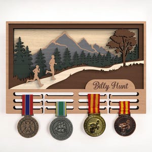 May include: Wooden medal display with a mountain and runner silhouette design. The display has four medals with colorful ribbons. The name "Billy Hunt" is engraved on the display. The background features a mountain scene with trees and runners.