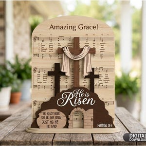 May include: Wooden Easter decoration featuring a cross with a draped cloth, set against a backdrop of musical notes. The words "Amazing Grace" and "He is Risen" are prominently displayed, along with the Bible verse Matthew 28:6.