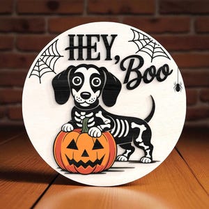 Könnte beinhalten: Runde Halloween-Dekoration aus Holz mit einem Dackel-Skelett-Hund und einem geschnitzten orangefarbenen Kürbis. Die Worte "HEY, Boo" stehen über dem Hund, mit Spinnweben und einer Spinne. Hintergrund: Backsteinmauer und Holzoberfläche.