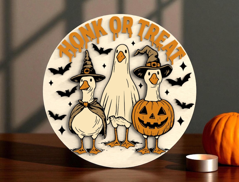 Puede incluir: Decoraci&oacute;n redonda de Halloween de madera con tres gansos de dibujos animados. Uno est&aacute; disfrazado de fantasma, otro lleva un sombrero de bruja y una capa, y el tercero est&aacute; con un disfraz de calabaza. Las palabras "HONK OR TREAT" est&aacute;n en la parte superior, con murci&eacute;lagos y estrellas.