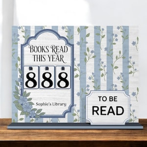 May include: A wooden book counter with the text "BOOKS READ THIS YEAR" and the number "888" displayed. The counter also has a "TO BE READ" sign. The background features a blue and white floral design. The text "Sophie's Library" is also displayed.