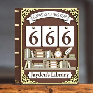 May include: A wooden book-shaped sign with the text "BOOKS READ THIS YEAR" at the top. It displays the number "666" on white flip cards. Below, a shelf with miniature books, a clock, and a quill. The sign is personalized with "Jayden's Library".