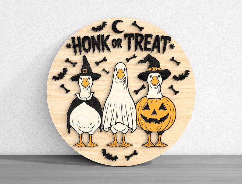 Puede incluir: Un letrero redondo de madera con tres gansos disfrazados para Halloween. Uno lleva un sombrero de bruja, otro una s&aacute;bana de fantasma y el tercero un disfraz de calabaza. El letrero dice "HONK OR TREAT" con murci&eacute;lagos, huesos y una luna.