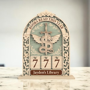 May include: Wooden book tracker with the text "BOOKS READ THIS YEAR" and "Jayden's Library". The design features a dragon, sword, and wings. The tracker displays the number 777. The frame has an ornate floral design.