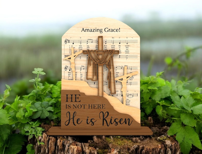 May include: Wooden religious decoration featuring three crosses, with the central cross draped with fabric. The background includes sheet music and the words "Amazing Grace!" The base reads "He is not here, He is Risen."