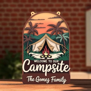May include: A layered wooden sign with a camping theme. The sign features a tent, campfire, palm trees, and the words "WELCOME TO OUR Campsite" and "The Gomez Family". The background shows a sunset.