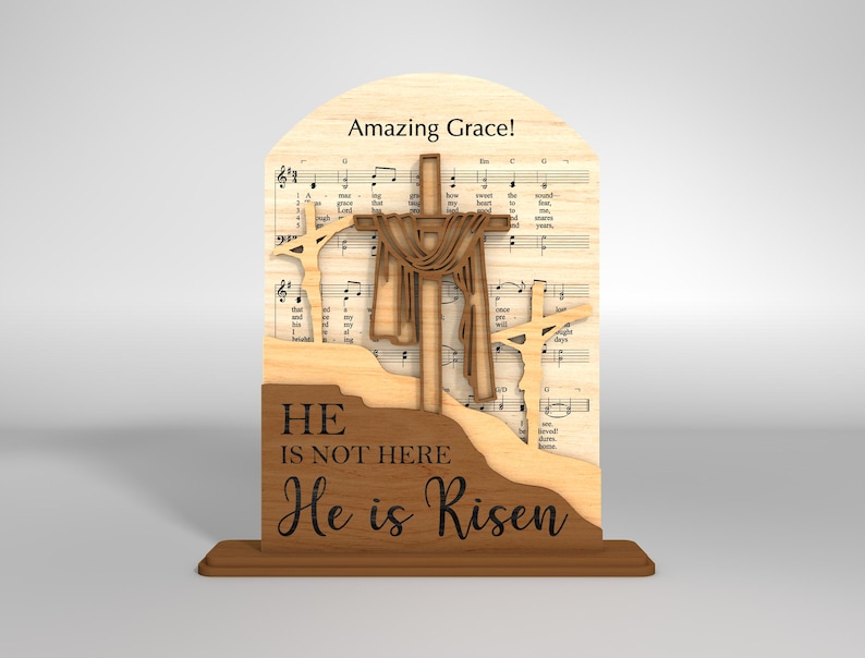 May include: Wooden Easter decoration featuring three crosses, with the central cross draped with fabric. The background includes sheet music and the words "Amazing Grace!" The base reads "He is not here, He is Risen."