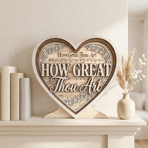 May include: A heart-shaped wooden sign featuring layered cutouts with the text "How Great Thou Art" in both serif and script fonts. The background displays printed musical notation. The sign has a light wood base and a dark wood inner border.