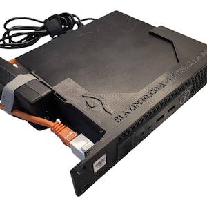May include: Black computer server with an attached power supply and orange Ethernet cable. The server has the text "BLAZINED.COM - OPTIPLEX MICRO" printed on the side. A black cable with a velcro strap is also attached.