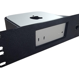 May include: A black rack mount for a Mac Mini computer. The rack has a rectangular design with a silver faceplate and a black frame. The Apple logo is visible on the top of the Mac Mini.