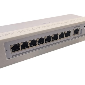 May include: A white network switch with multiple Ethernet ports. The device has a rectangular shape with a series of black ports and the text "USW-FLEX-2.5G-8 BLAZING" printed on the top. It is designed for rack mounting.