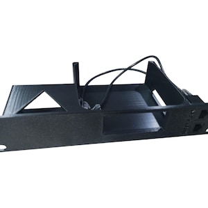 May include: A black 3D-printed rack mount bracket featuring a rectangular frame with a triangular cutout on the left side, a central open compartment, and two integrated Ethernet ports on the right side with connected black network cables.