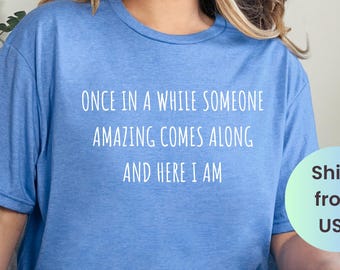 May include: A blue t-shirt with the text "ONCE IN A WHILE SOMEONE AMAZING COMES ALONG AND HERE I AM" in white. The shirt is a heather true royal color. The image also includes the text "Ships from USA".