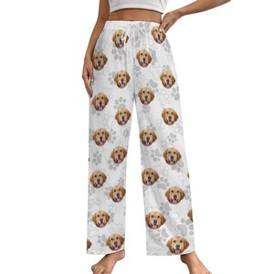 May include: White pajama pants featuring a repeating pattern of golden retriever faces and paw prints. The pants have a drawstring waist and a relaxed fit, suitable for lounging or sleeping. The design is playful and dog-themed.