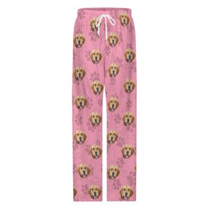 May include: Pink pajama pants featuring a repeating pattern of golden retriever faces and paw prints. The pants have a drawstring waist and a relaxed fit, perfect for lounging. The fabric appears soft and comfortable.