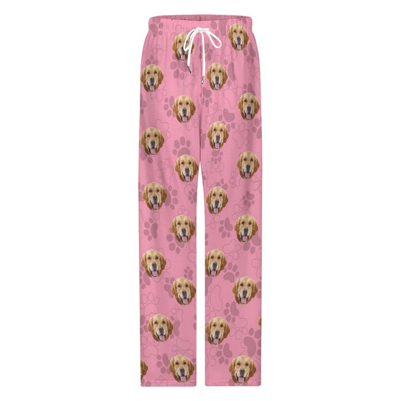 May include: Pink pajama pants featuring a repeating pattern of golden retriever faces and paw prints. The pants have a drawstring waist and a relaxed fit, perfect for lounging. The fabric appears soft and comfortable.