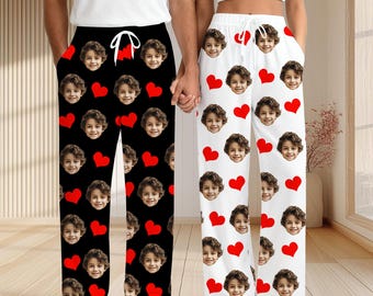 May include: Matching pajama pants, one pair black and one pair white, each featuring a repeating pattern of red hearts and a smiling face. The black pants have a white drawstring, and the white pants have a red drawstring.