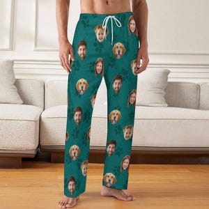 May include: Teal pajama pants featuring a repeating pattern of faces and paw prints. The faces include a mix of people and golden retrievers. The pants have a drawstring waist.
