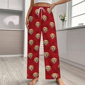 May include: Red pajama pants featuring a repeating pattern of Golden Retriever faces and paw prints. The pants have a drawstring waist and a relaxed fit, perfect for lounging. The fabric appears soft and comfortable.