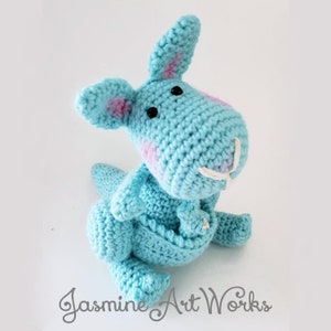 May include: A crocheted blue kangaroo with pink accents and black eyes. The kangaroo is sitting with its legs tucked under its body.