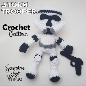 以下が含まれることがあります： 黒のディテールが付いた白い編みぐるみストームトルーパー人形が、黒の編みぐるみブラスターを持っています。人形は白い表面に立っています。人形の上に「Stormtrooper Crochet Pattern」というテキストが書かれています。