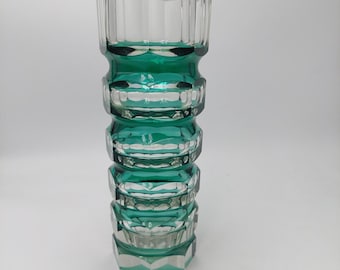 Könnte beinhalten: Eine klare Glasvase mit geometrischem Design und einem tealgrünen Farbton. Die Vase hat eine zylindrische Form mit einer Reihe von gestapelten, sechseckigen Abschnitten. Die Oberseite der Vase ist offen und das Glas hat eine gerippte Textur.