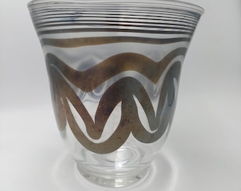 Könnte beinhalten: Transparente Glasvase mit ausgestellter Form. Die Vase hat horizontale schwarze Streifen am Rand und wellenförmige, bronzefarbene Muster auf dem Körper. Das Design verleiht der Vase einen Vintage- oder Art-Deco-Look.