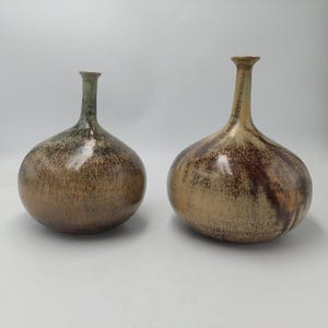Könnte beinhalten: Zwei Keramikvasen mit bauchigem Körper und schlankem Hals. Die Vasen haben eine gesprenkelte braune und beige Glasur mit einem grünen Farbton am Hals. Die Vasen sind in Form und Größe ähnlich.