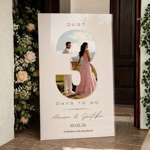 May include: A rectangular wedding countdown sign with a large cutout of the number 3 revealing a photo of a couple. The sign features the text JUST 3 DAYS TO GO, the names Aman & Geetika, the date 10.02.26, and the phrase A lifetime waits just ahead.