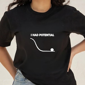 May include: Black crew neck t-shirt featuring the white text "I HAD POTENTIAL" above a graphic of a ball rolling down a ramp. The graphic ends with the ball at the bottom. The shirt is black.