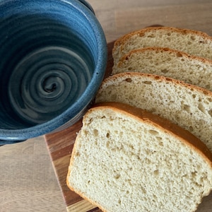 Puede incluir: Cuatro rebanadas de pan blanco en una tabla de cortar de madera junto a un taz&oacute;n de cer&aacute;mica azul.