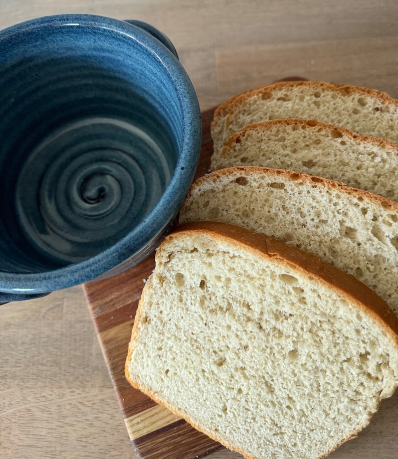 Puede incluir: Cuatro rebanadas de pan blanco en una tabla de cortar de madera junto a un taz&oacute;n de cer&aacute;mica azul.