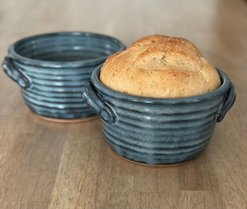 Puede incluir: Dos cuencos de pan de cer&aacute;mica azul con una hogaza de pan en uno de los cuencos. Los cuencos tienen un dise&ntilde;o a rayas y asas.