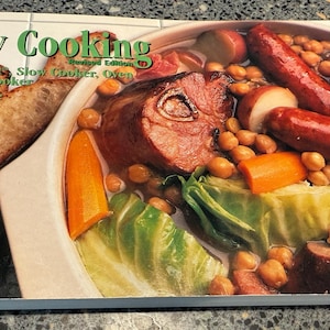 May include: A cookbook titled "Slow Cooking" with a photo of a stew with sausage, carrots, and chickpeas. The cover also features text that reads "In Crock-Pot, Slow Cooker, Oven and Multi Cooker" and the author's name, Joanna White.