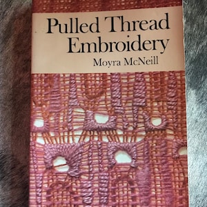 May include: A vintage book titled "Pulled Thread Embroidery" by Moyra McNeill. The cover features a close-up of embroidered fabric in shades of red and brown, with the title in black text on a tan background.