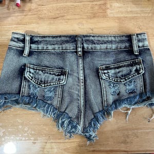 Puede incluir: Un par de pantalones cortos de mezclilla con dobladillo deshilachado y detalles desgastados. Los pantalones cortos tienen dos bolsillos en la parte posterior y un cierre de bot&oacute;n y cremallera en la parte delantera.