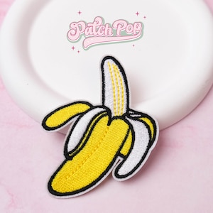 Pode incluir: Patch bordado com um design de banana descascada. A banana é amarela com detalhes brancos e pretos. O patch tem o texto "Patch Pop" em rosa.